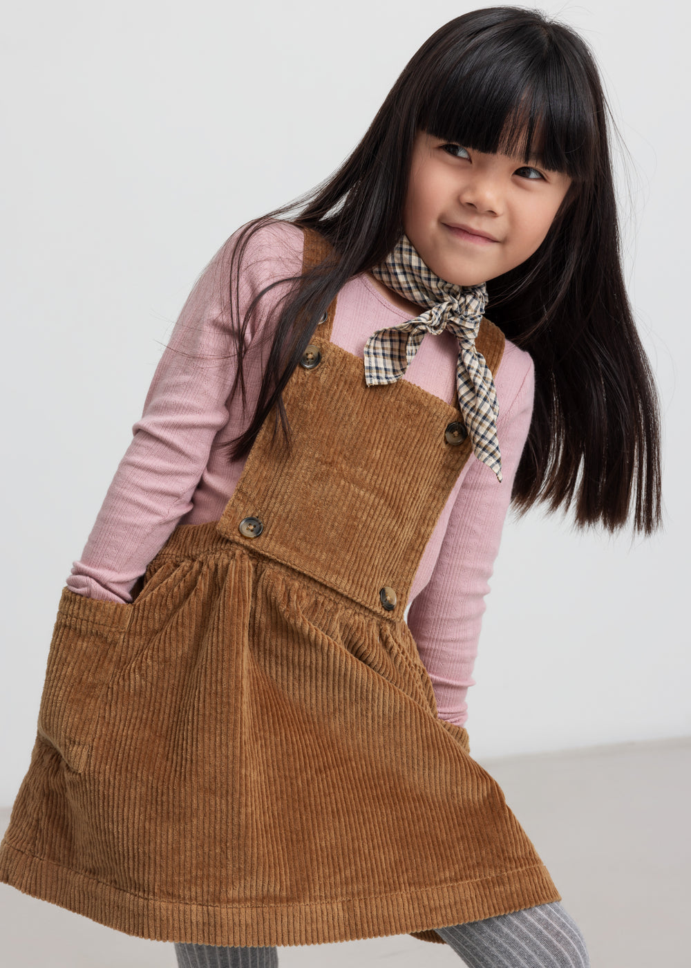 Pige iført rosa pointelle bluse og brun kjole med seler