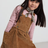 Pige iført rosa pointelle bluse og brun kjole med seler