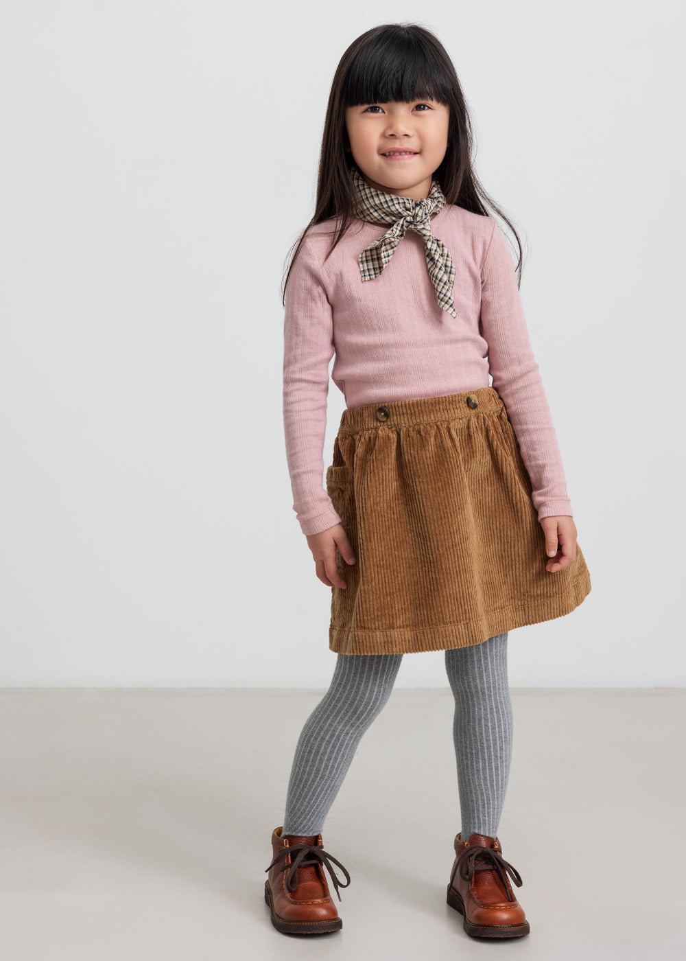 Pige iført rosa pointelle bluse og brun nederdel