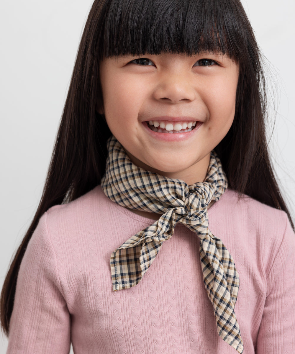 Pige med brun ternet tørklæde bundet om halsen og lyserød t-shirt