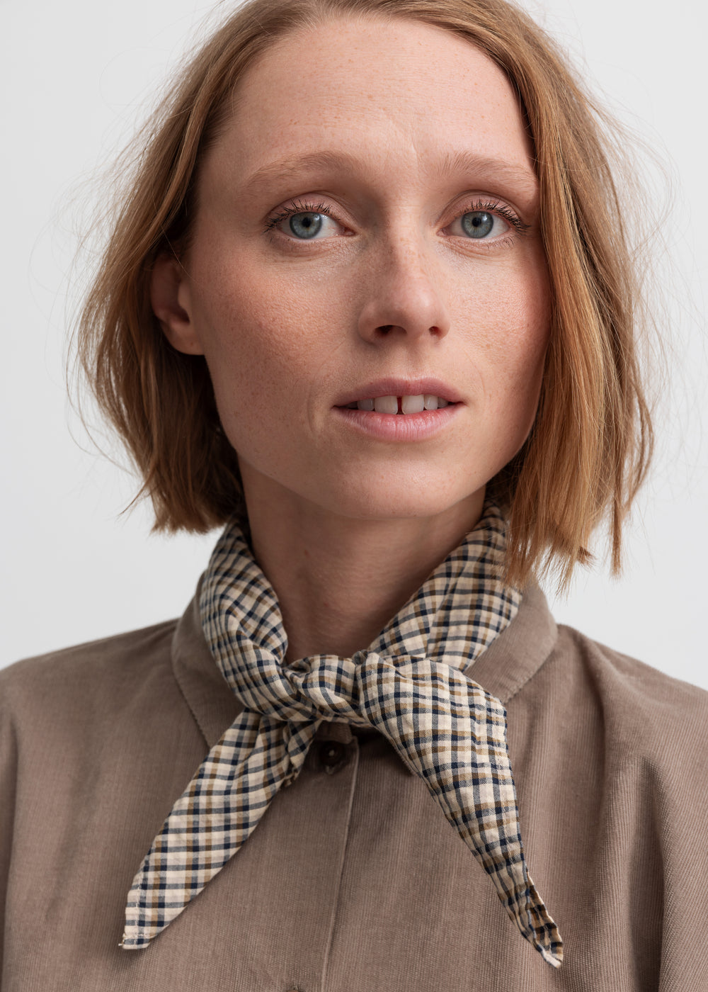 Kvinde i beige skjorte med ternet tørklæde om halsen