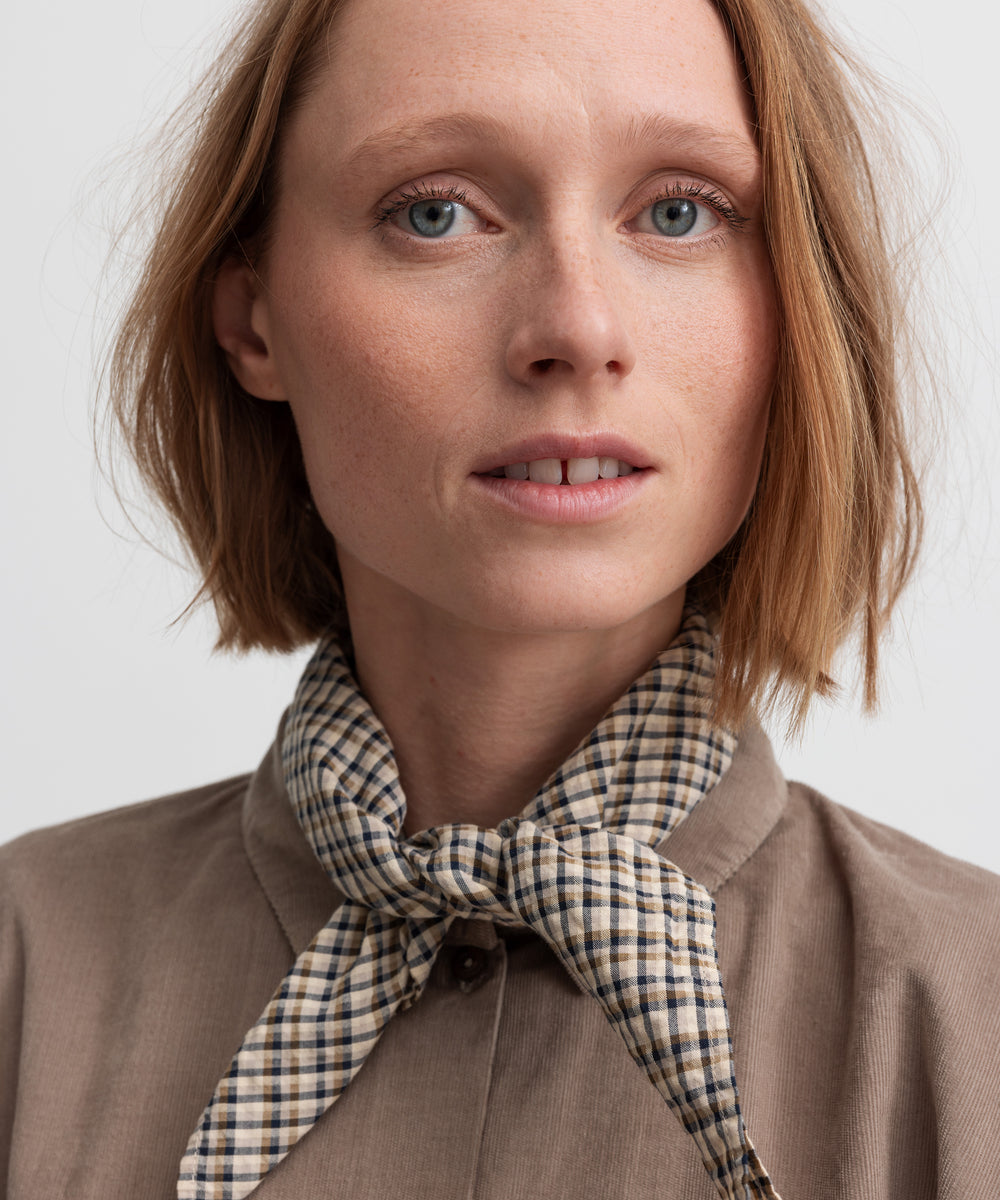 Kvinde iført brun ternet tørklæde bundet om halsen