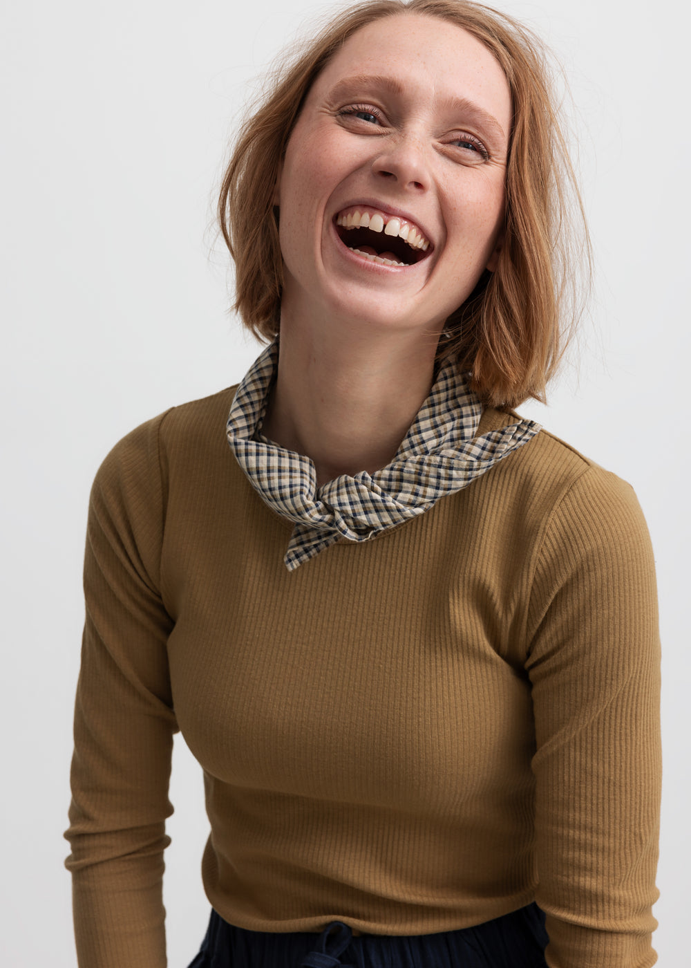 Glad kvinde iført langærmet brun ribstrikket t-shirt 