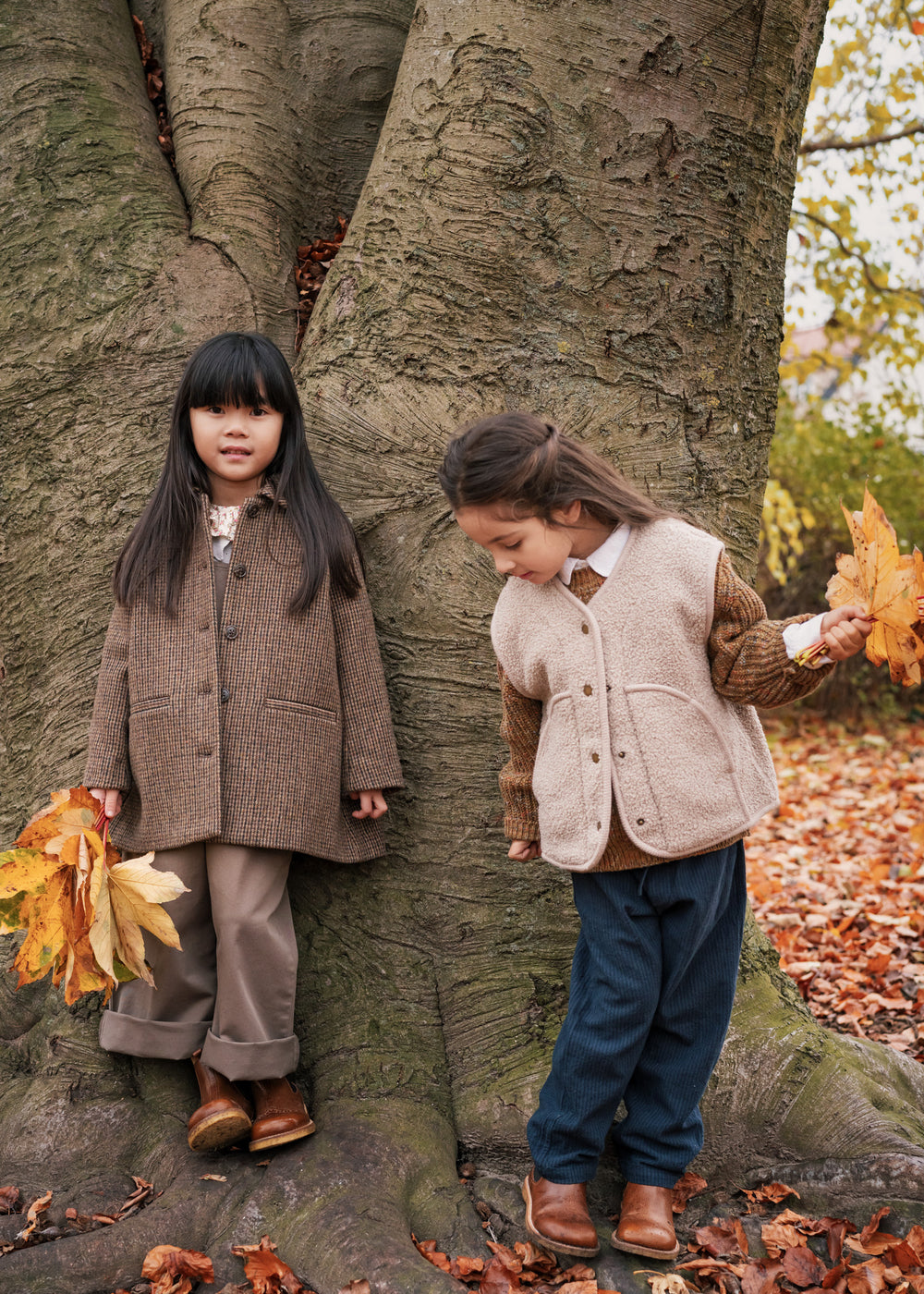 Børn iført efterårsjakker står ved et træ