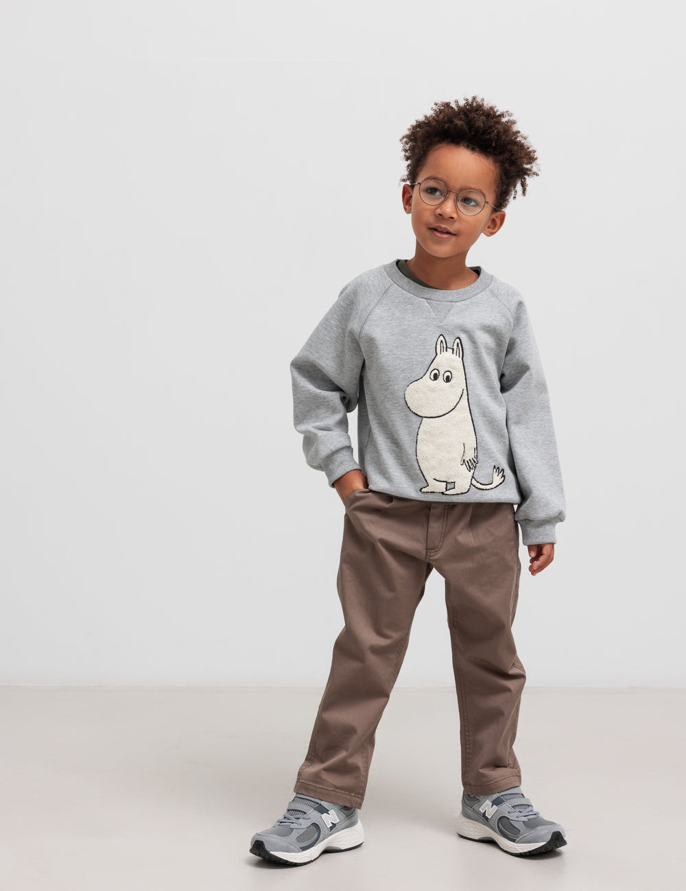Barn iført grå Moomin-trøje med rund hals og brune bukser