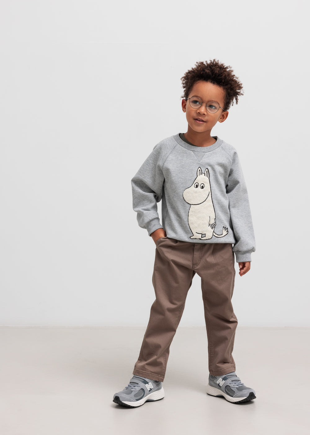 Barn iført grå Moomin-trøje med rund hals og brune bukser