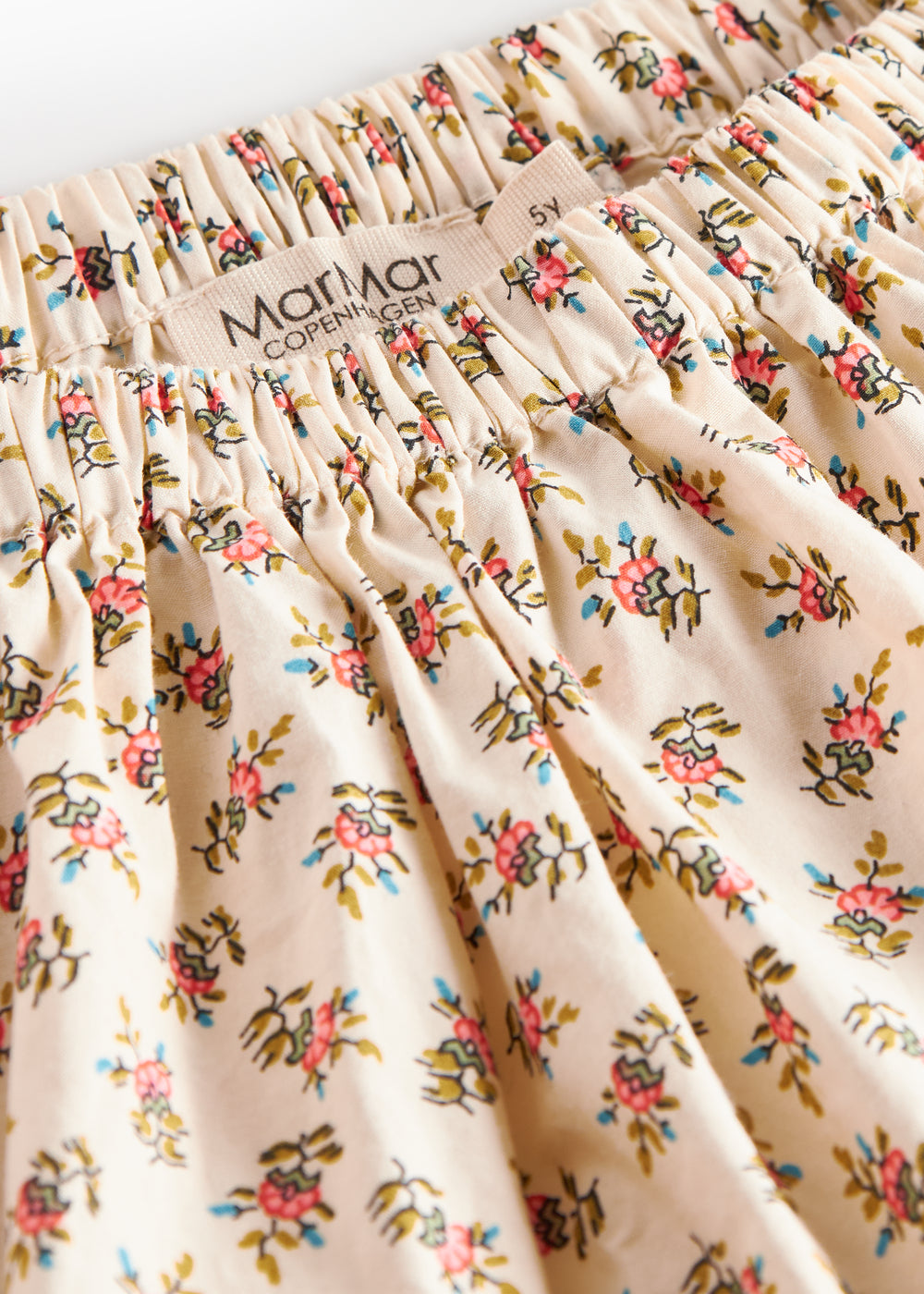 Nærbillede af stof med blomstermønster og flæsekant på nederdel