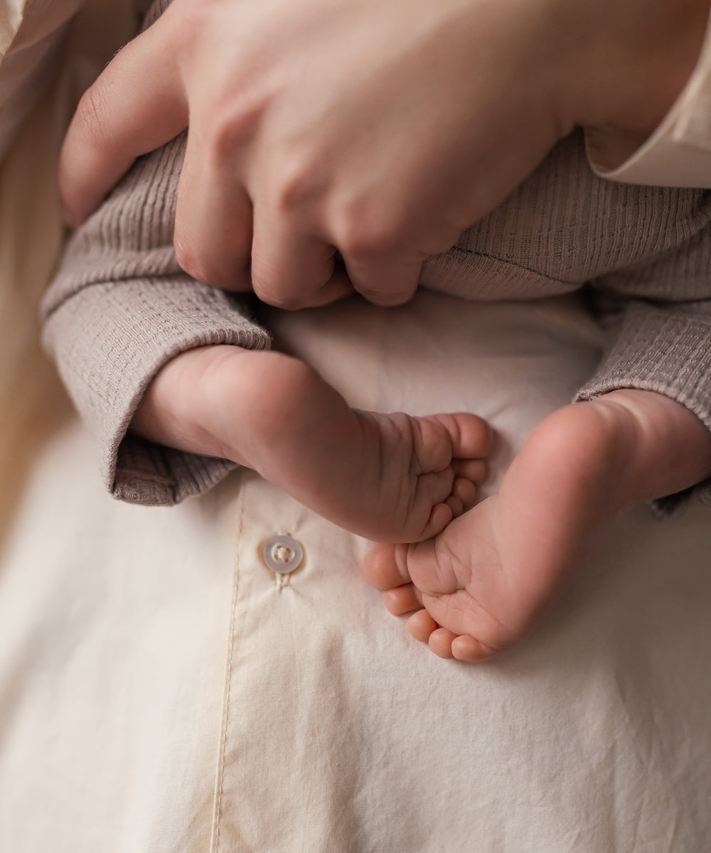 Nærbillede af babyfødder holdt af kvinde iført cremefarvet bluse