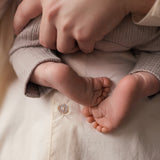 Mor holder nyfødt iført beige pointelle hue og sparkedragt