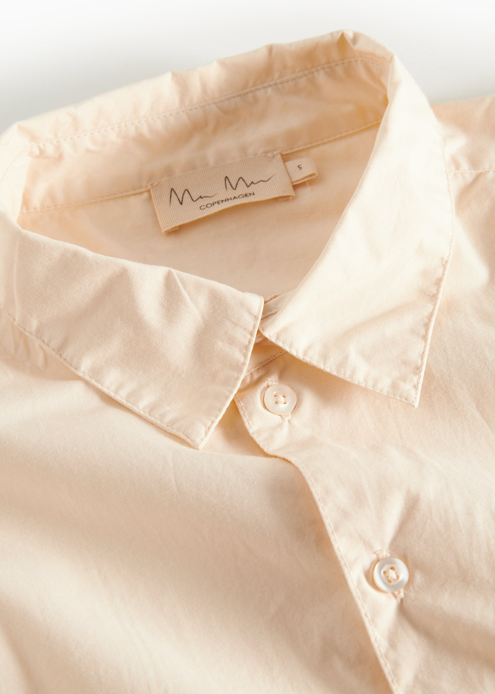 Detaljebillede af krave på cremefarvet bluse