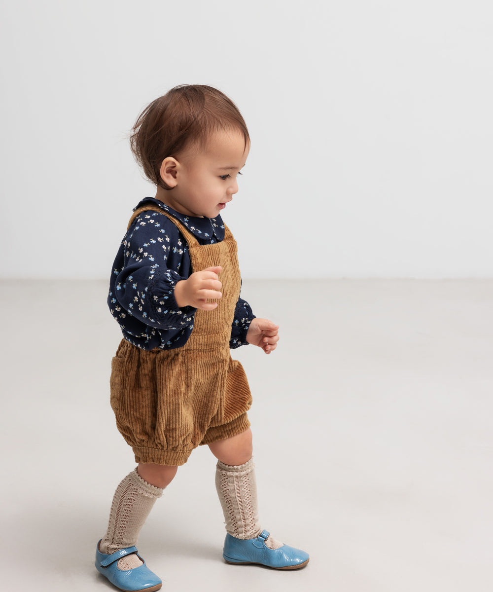 Baby iført brun fløjlsshorts med seler og mørkeblå bluse