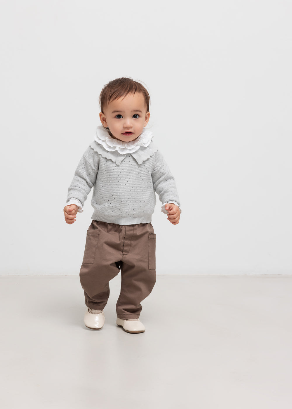 Lille barn iført grå strikbluse og brune bukser står op