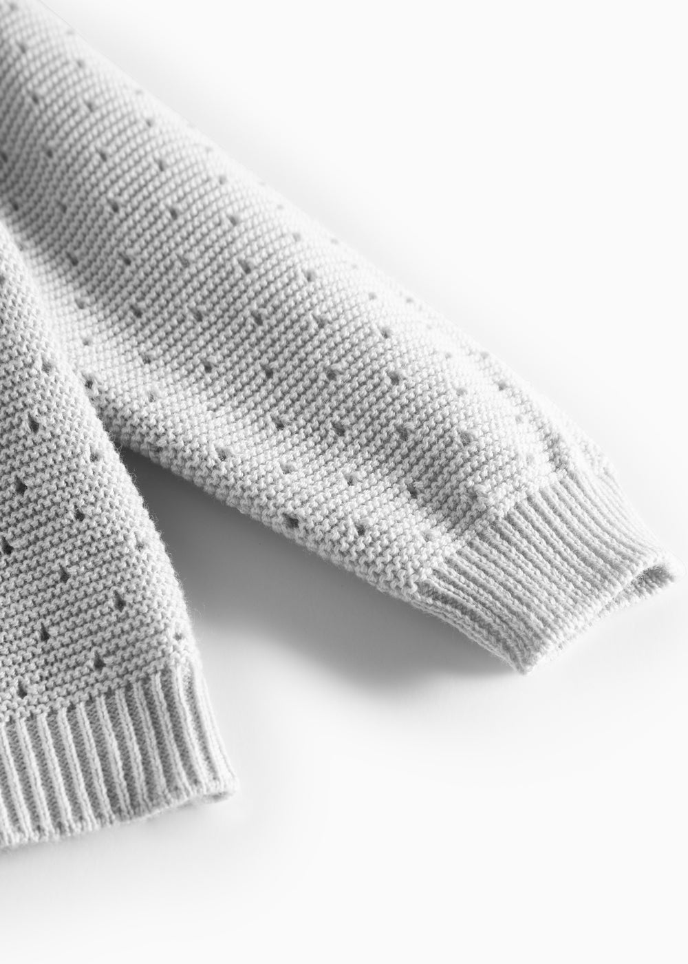 Detalje af ærme med hulmønster på grå strikbluse