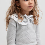 Pige med grå strikbluse med flæsekrave og mønstret nederdel