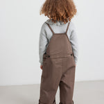 Pige iført brune selebukser og grå strikbluse set bagfra