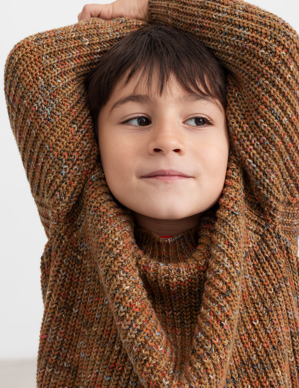 Dreng med brunmeleret striktrøje og hænder bag hovedet