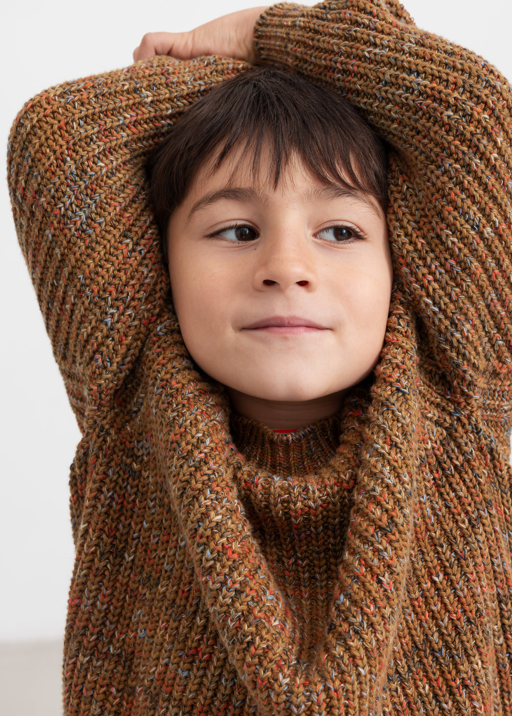 Dreng med brunmeleret striktrøje og hænder bag hovedet