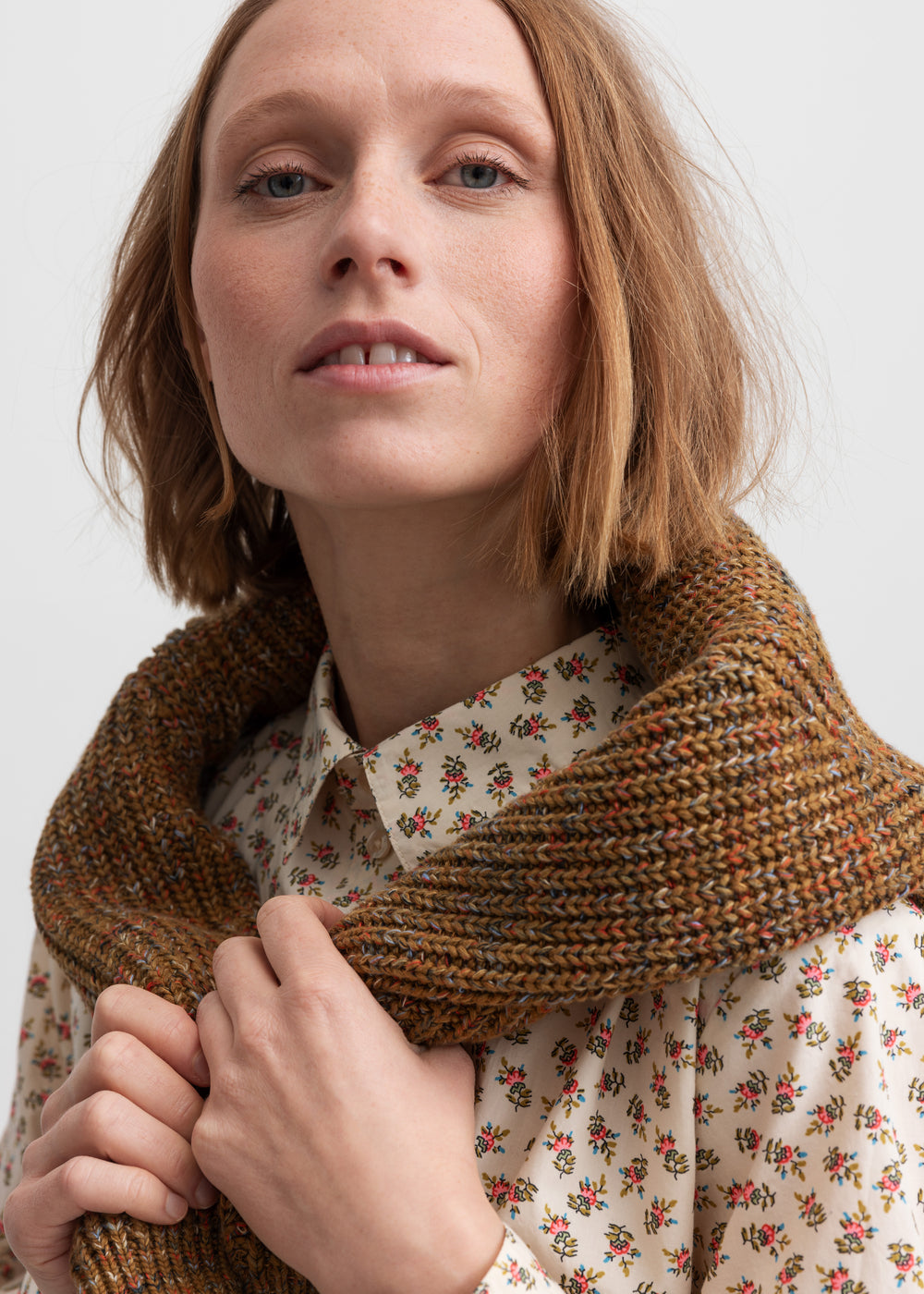 Kvinde iført brunmeleret striktrøje og blomstret skjorte