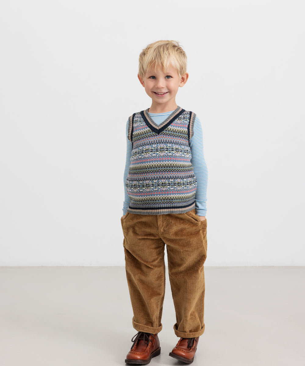 Dreng i brun buks og farverig strikvest med V-hals