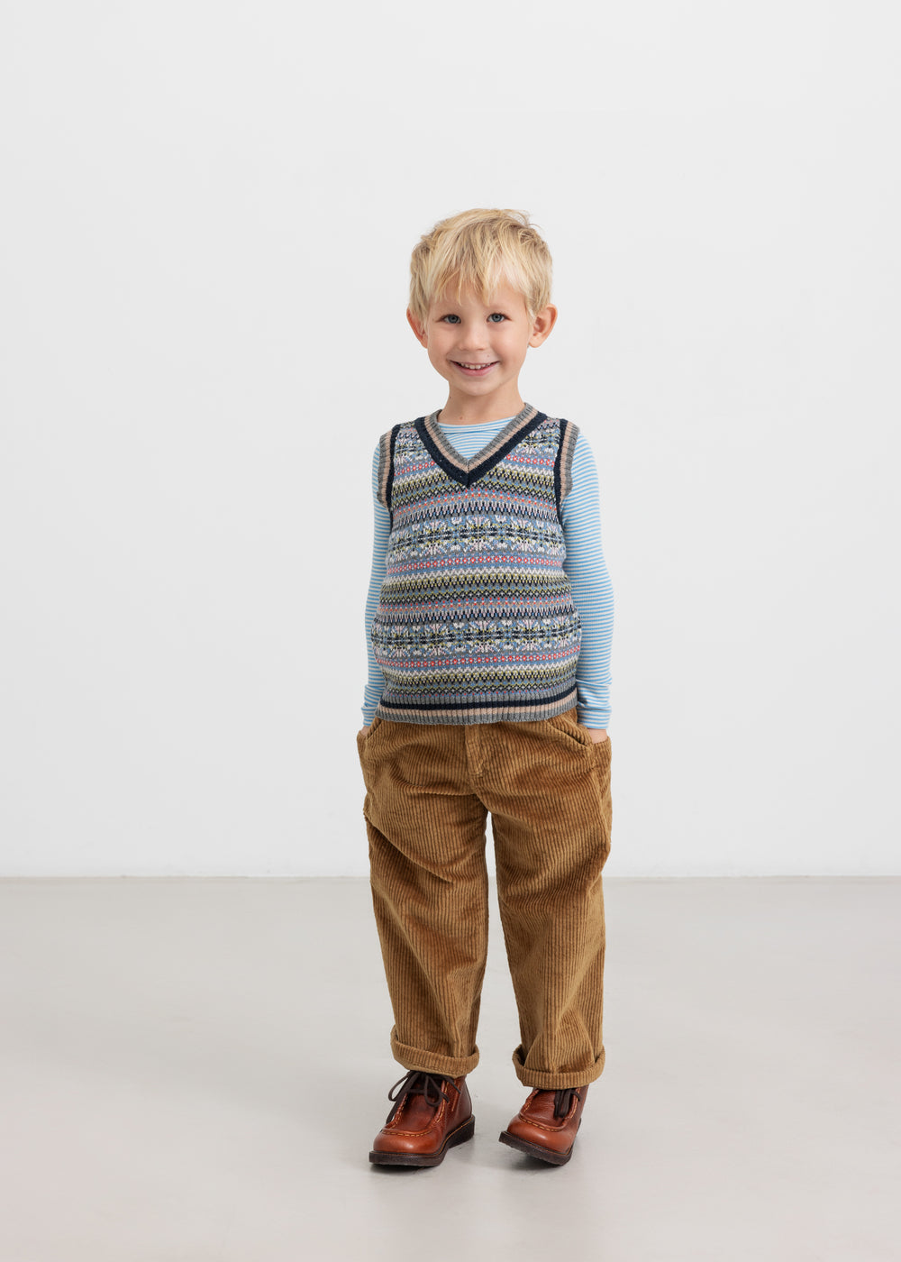 Dreng iført blå og hvid stribet bluse med mønstret strikvest og brune bukser