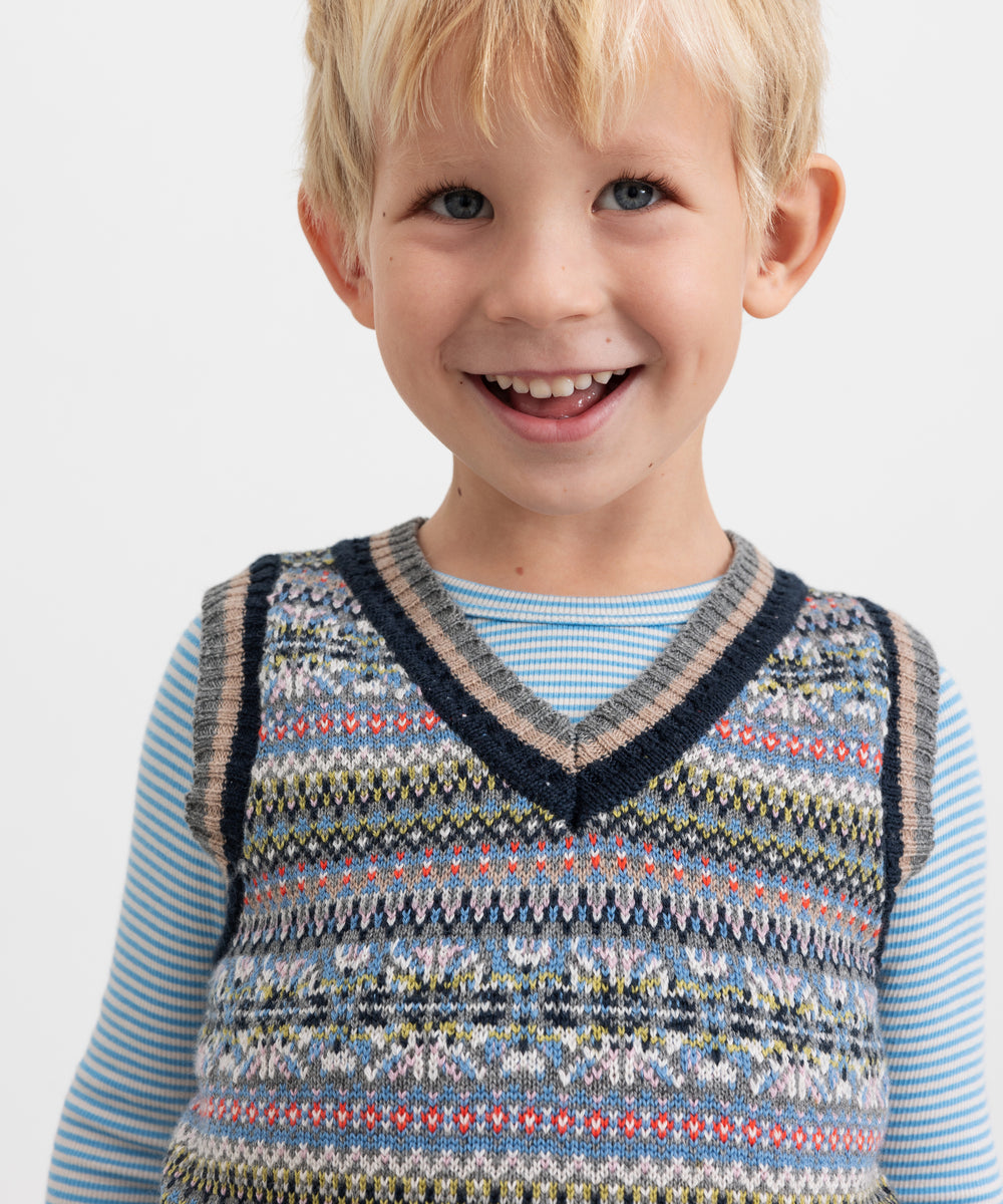 Dreng iført mønstret strikvest over lyseblå bluse