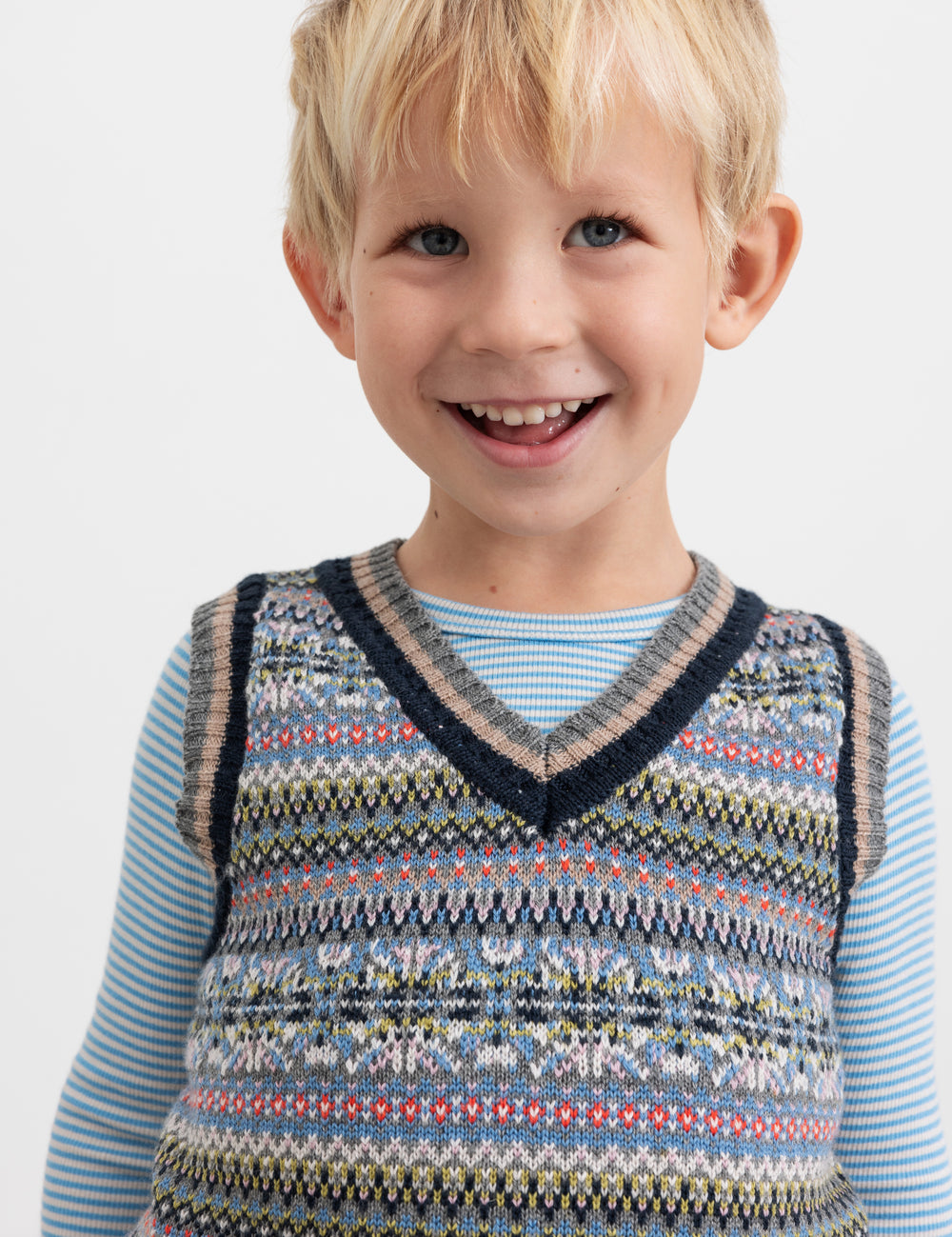 Smilende dreng iført blå og hvid stribet bluse under mønstret strikvest.