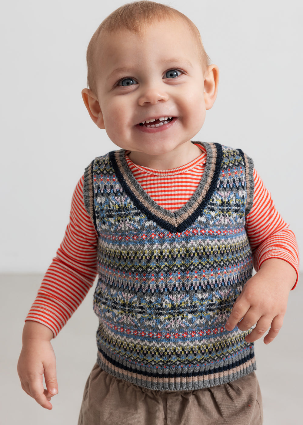Baby iført mønstret strikvest over stribet bluse