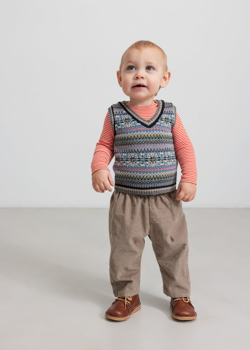 Baby iført beige babyfløjl­sbukser og mønstret strikvest