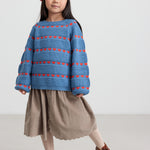 Børn iført blå striktrøje med røde hjerter, kombineret med brun nederdel og rød hue