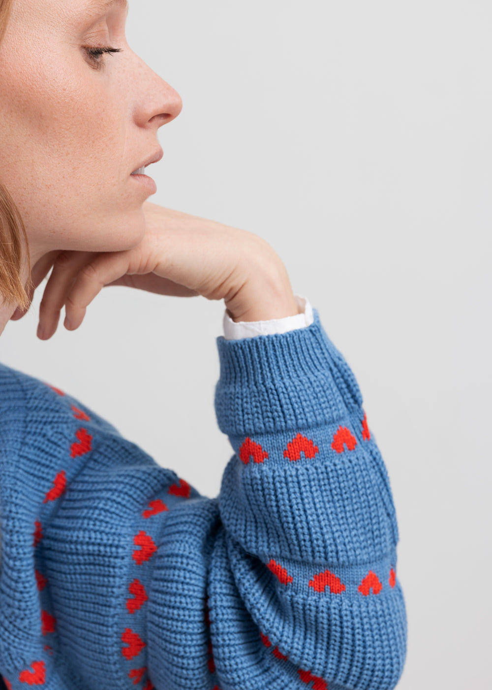 Kvinde iført blå striktrøje med røde hjerter og lange ærmer