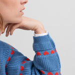 Kvinde iført blå striktrøje med røde hjerter og lange ærmer