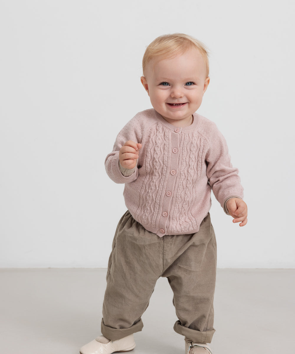 Baby i beige babyfløjl­sbukser og lyserød trøje