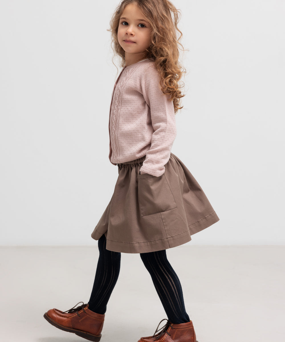 Børn iført lyserød strikcardigan med brun nederdel, set fra siden