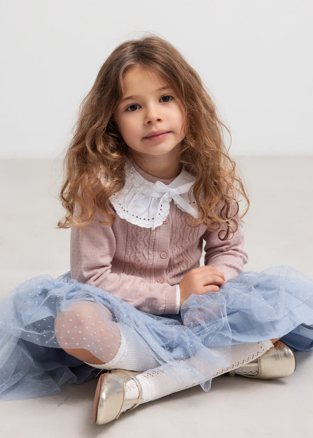 Pige sidder iført blå tylnederdel med prikmønster og bluse