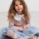 Pige sidder iført blå tylnederdel med prikmønster og bluse