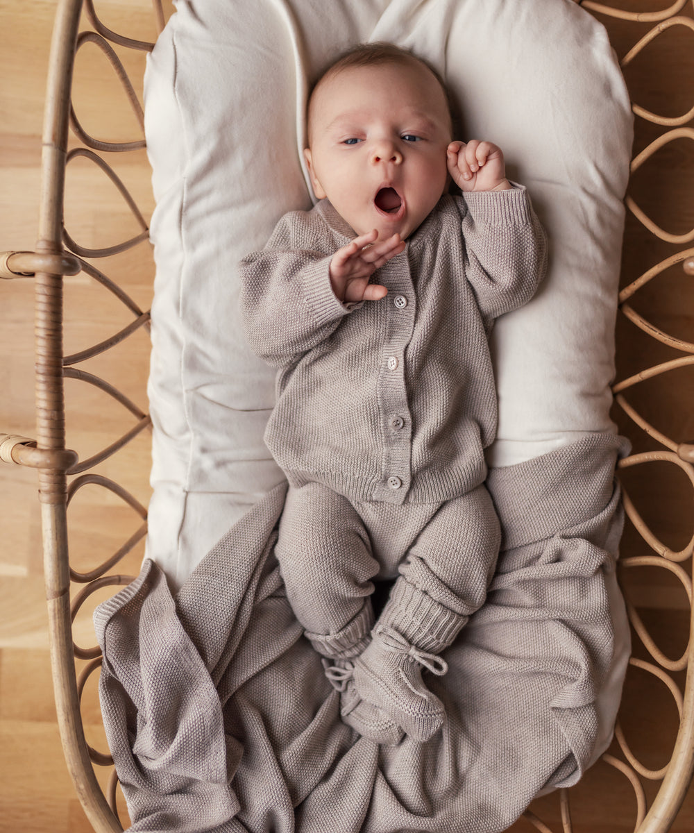 Baby med åben mund i beige strikket sæt liggende i kurv