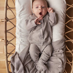 Baby iført beige/grå strikket sæt liggende i flettet kurv med beige tæppe