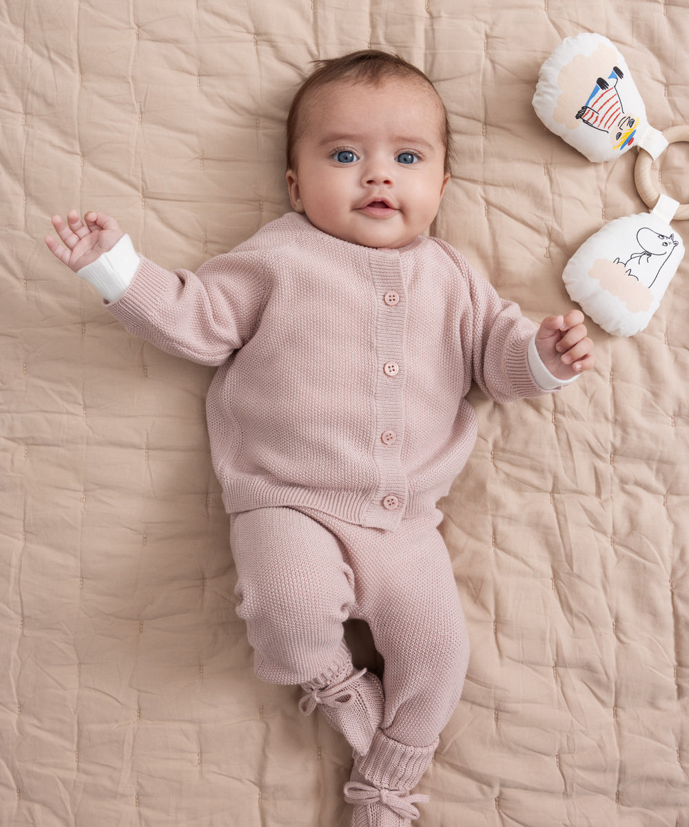 Baby iført lyserødt strikket sæt liggende på beige quiltet tæppe