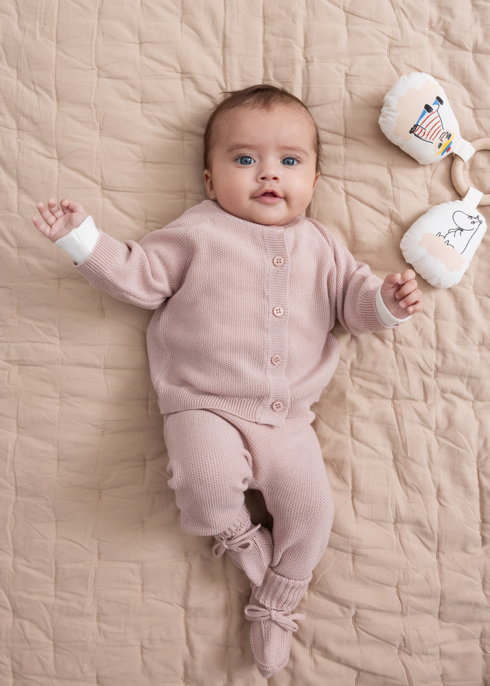Baby iført lyserødt strikket sæt liggende på beige quiltet tæppe