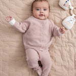 Baby iført lyserødt strikket sæt liggende på beige quiltet tæppe