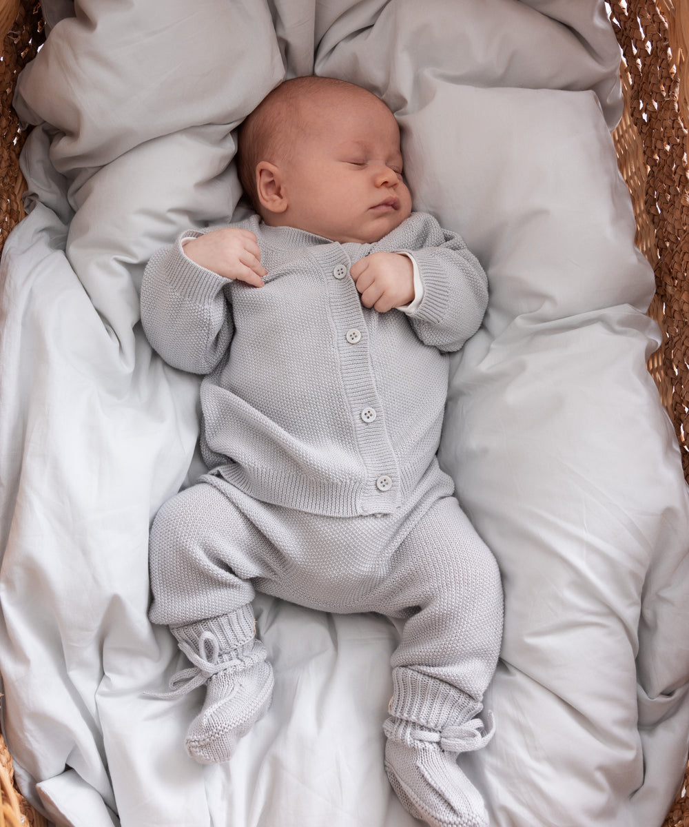 Sovende baby i lys grå strikket sæt liggende i kurv