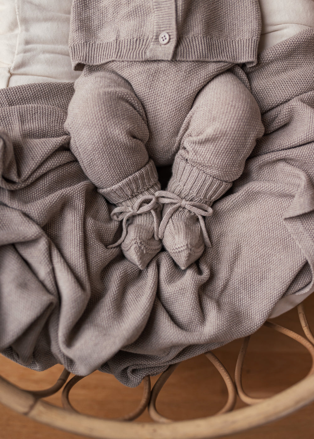 Baby iført beige strikket sæt med trøje og bukser liggende i kurv