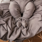 Baby iført beige strikket sæt med trøje og bukser liggende i kurv