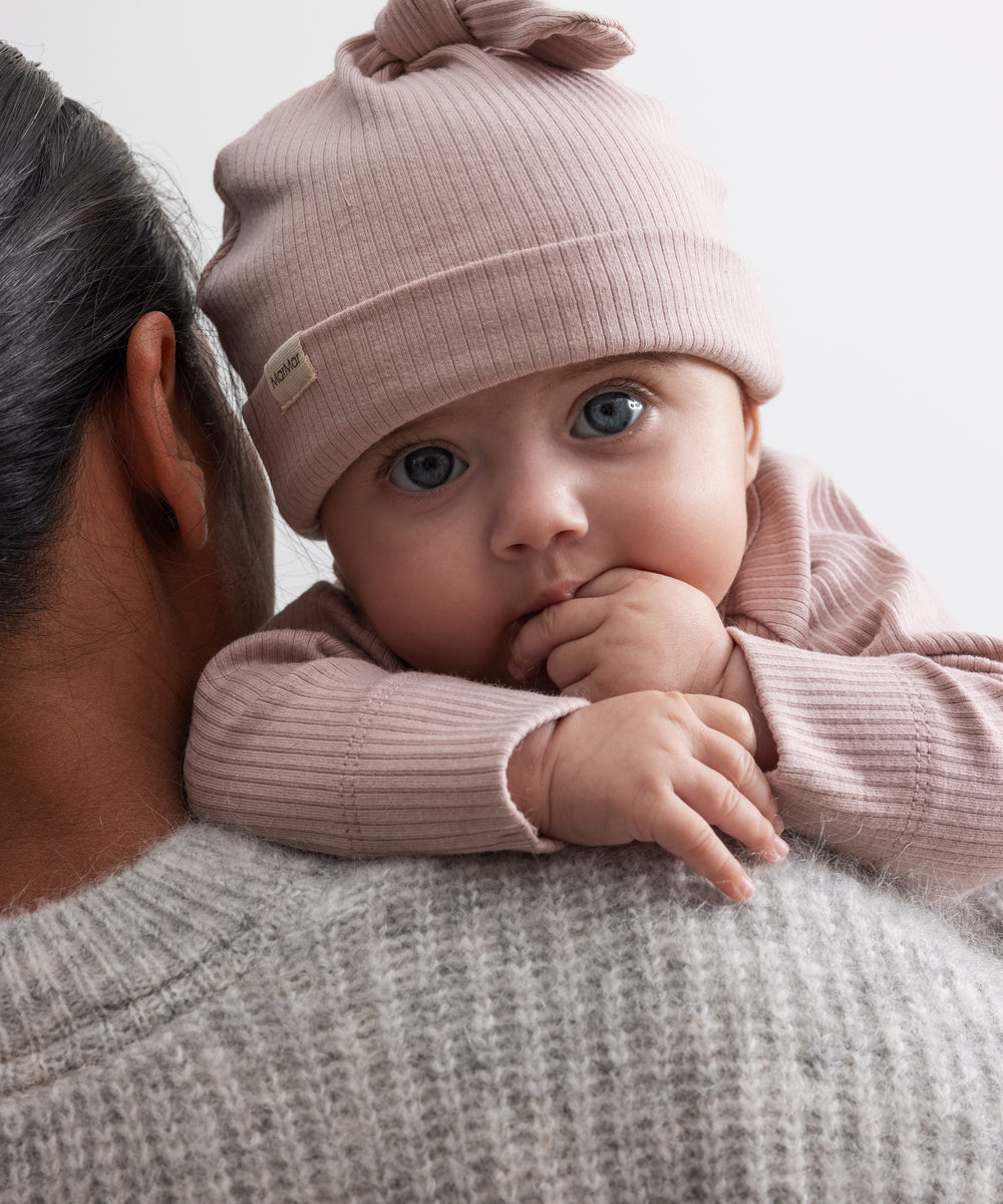 Baby iført lyserød ribstrikket babyhue med knude på toppen og opbukket kant