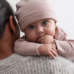 Baby iført lyserød ribstrikket babyhue med knude på toppen og opbukket kant