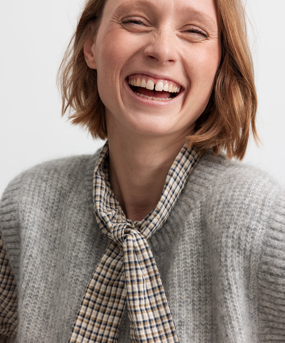 Kvinde smilende i grå strikvest i uld med skjorte under