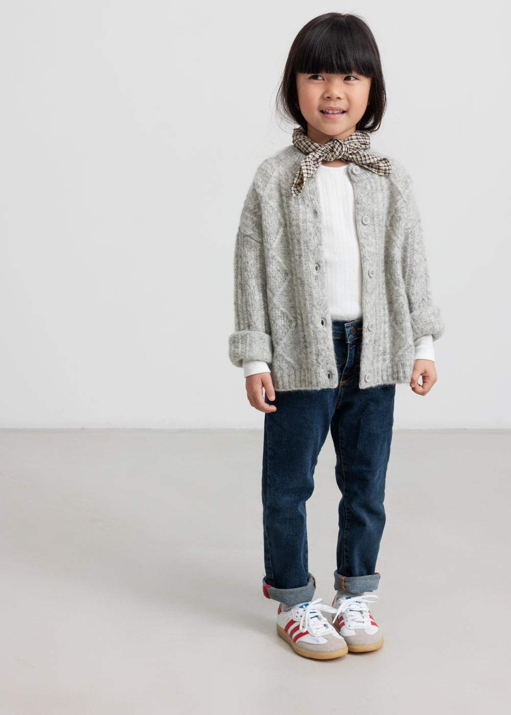 Barn iført brun ternet tørklæde og grå cardigan