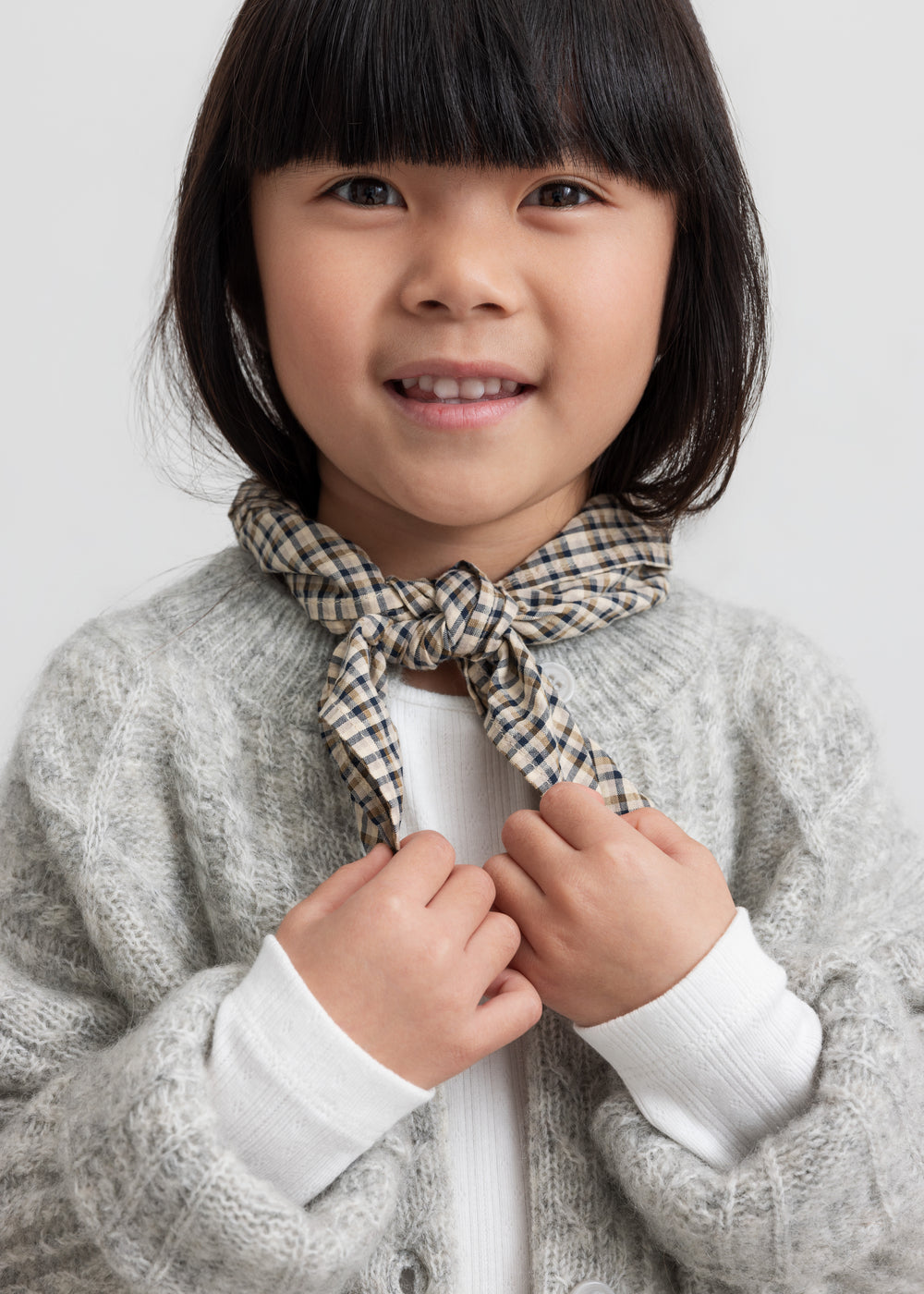 Pige iført hvid pointelle bluse, grå cardigan og ternet tørklæde