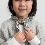 Pige iført hvid pointelle bluse, grå cardigan og ternet tørklæde