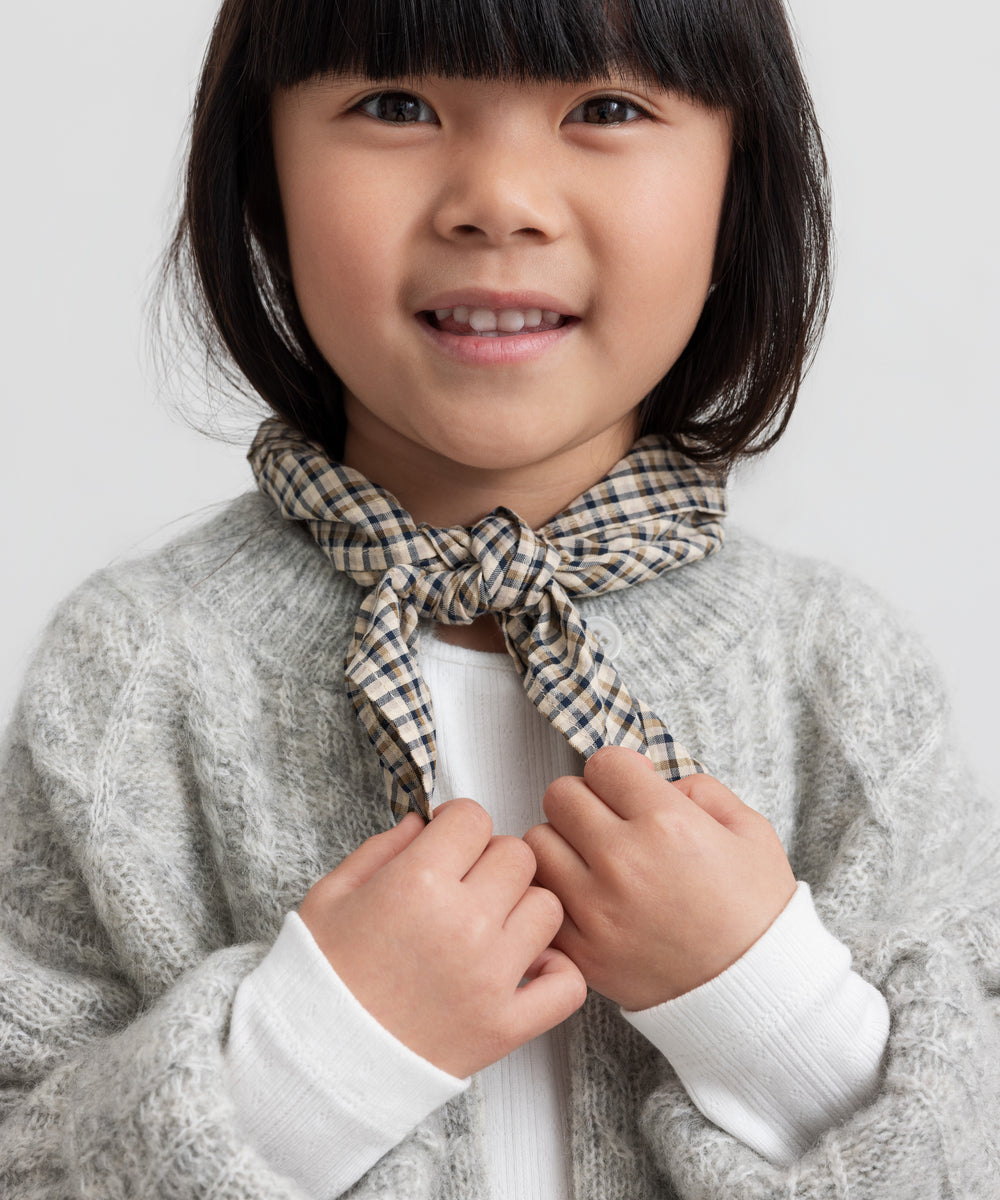 Pige iført lysegrå cardigan med ternet tørklæde